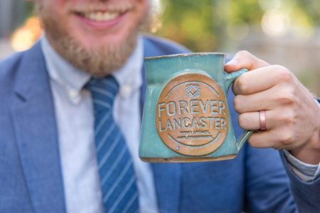 Man holds up Forever Lancaster mug