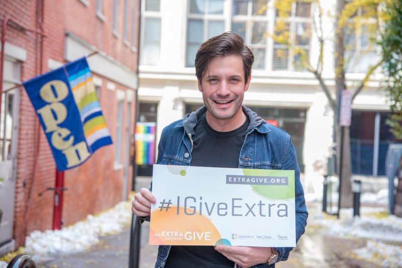 Man smiles and holds Extra Give sign