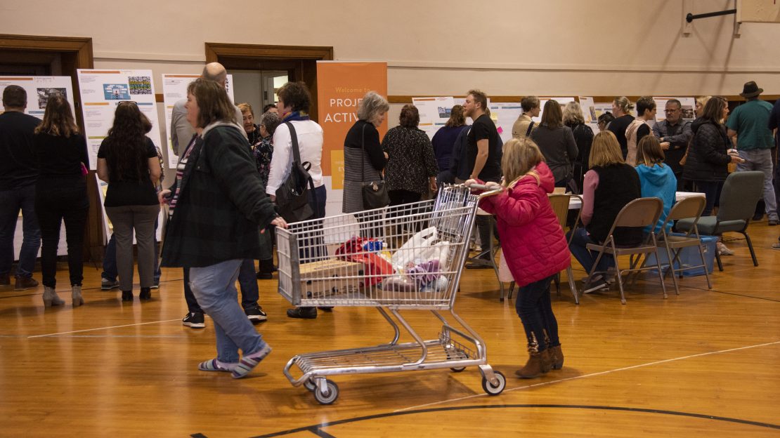 Group of people looking at poster boards. Small child with shopping cart is in center frame