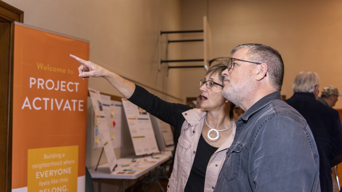 Two people stand next to each other while woman points at something in front of her