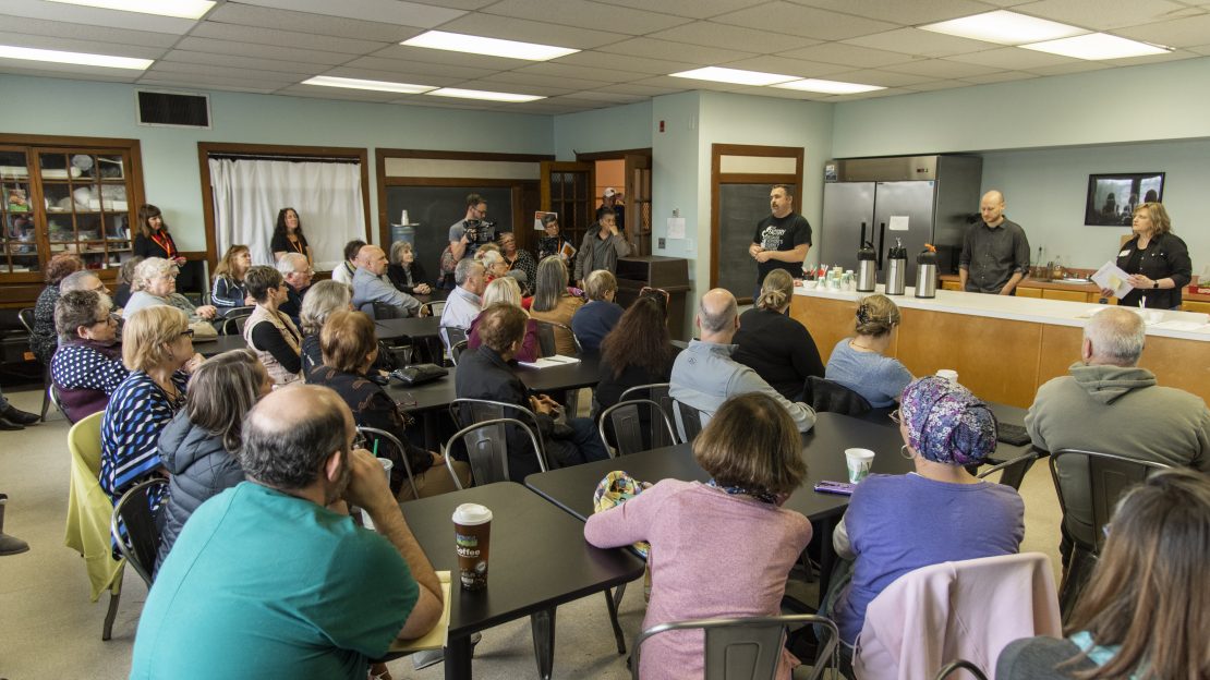 Room of people sitting at tables while three people present