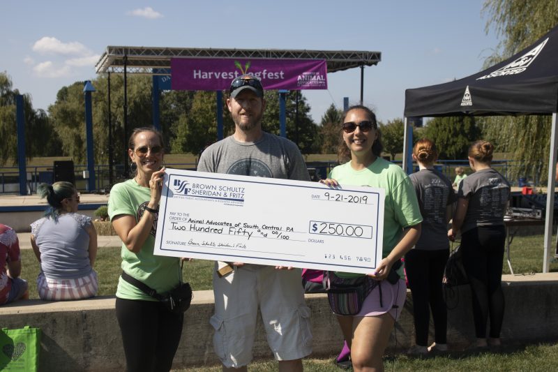 Three people stand outside holding a large check