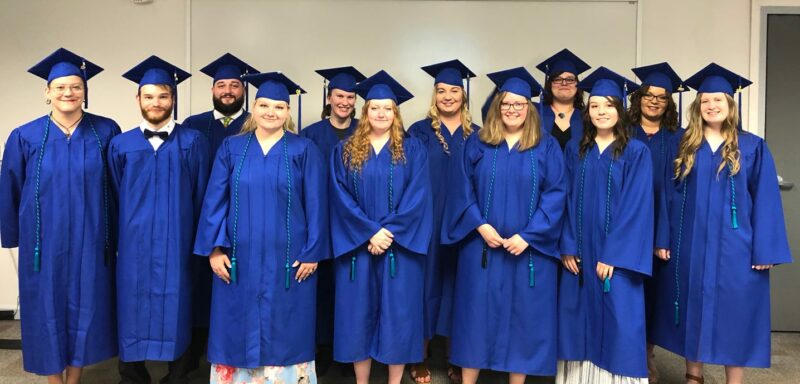 A group of students in blue graduation robes and hats look at the camera