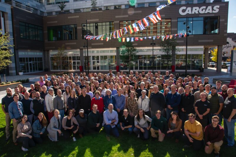 A group of Cargas employees stand outside their building on a sunny day.