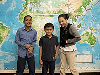 Three students stand in front of a world map