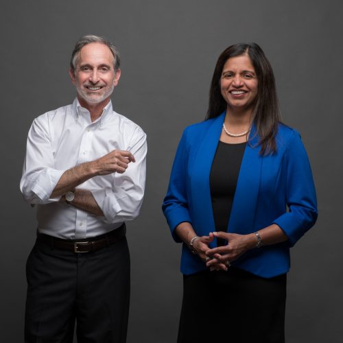 Two people in professional attire look at the camera, smiling.