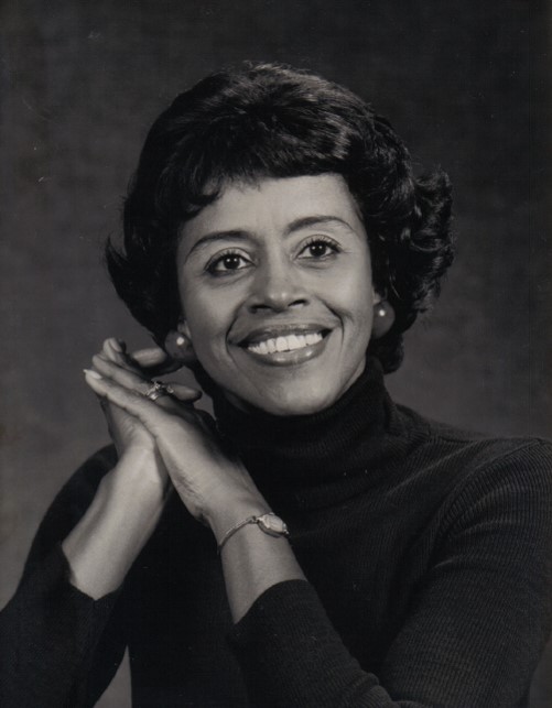 This picture shows Hazel smiling at the camera. She is posing with her hands clasped near her face. The picture is in black and white.