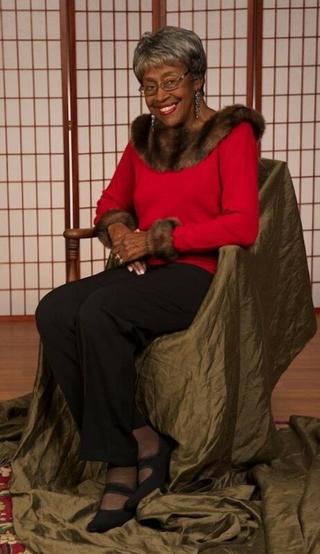 Hazel Jackson sits in a chair, wearing a red shirt. She is smiling.