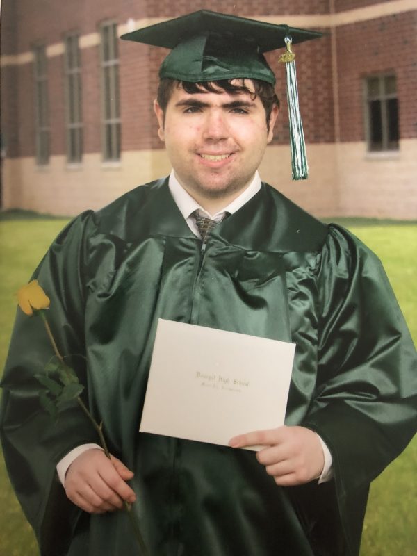 A photo of Bobby wearing his graduation robe and hat, looking at the camera and smiling. 