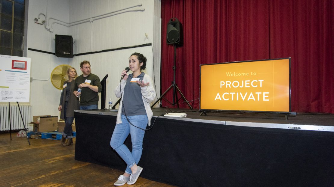 Woman stands in front of a stage with a project activate sign