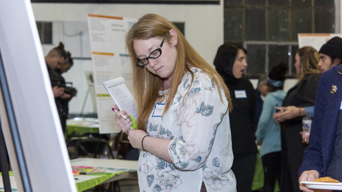 Woman holds notebook while looking at poster board