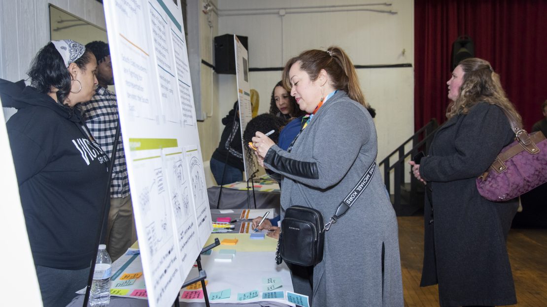 Group of people stand around poster board and table
