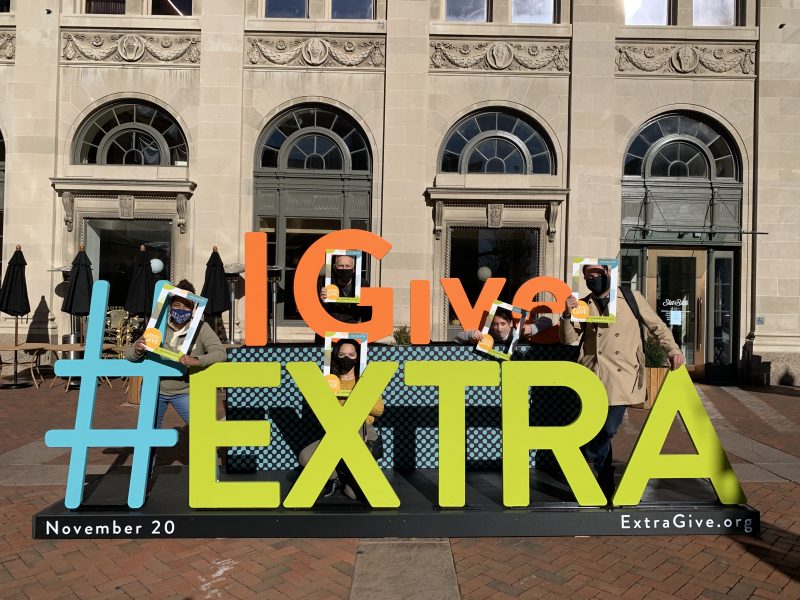 Five people posing around a large #IGiveExtra sign