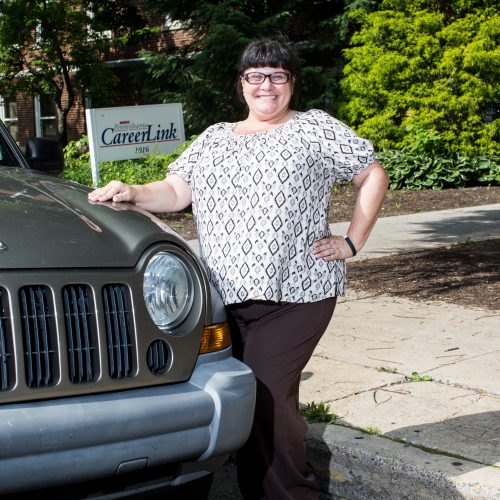 Woman stands next to a car with her hand on the hood