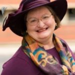 A picture of Patti Spencer, lawyer, looking at the camera and smiling. She has a fabulous hat and scarf.