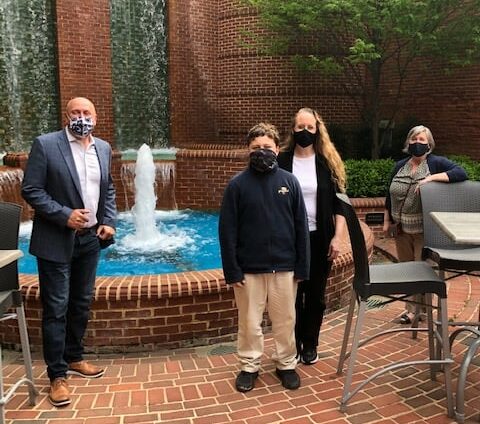 A group of people stand in front of a fountain. They are wearing masks.