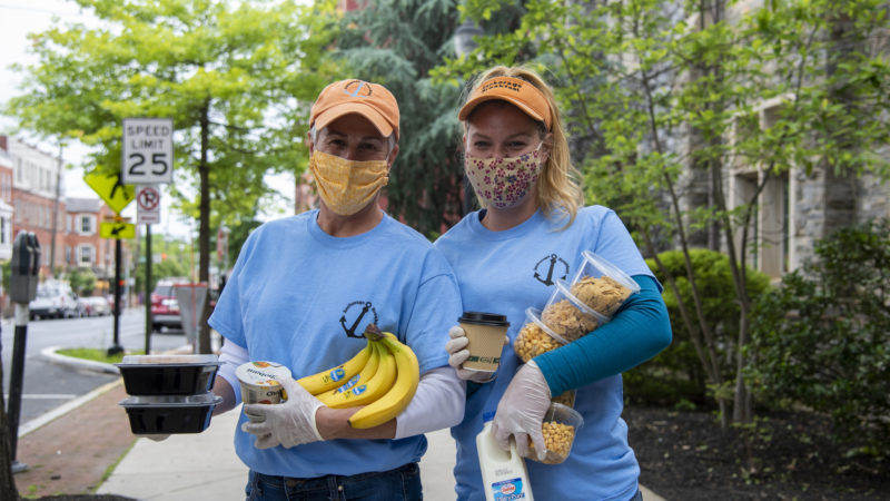 Two masked women smile at the camera while holding packages of food.