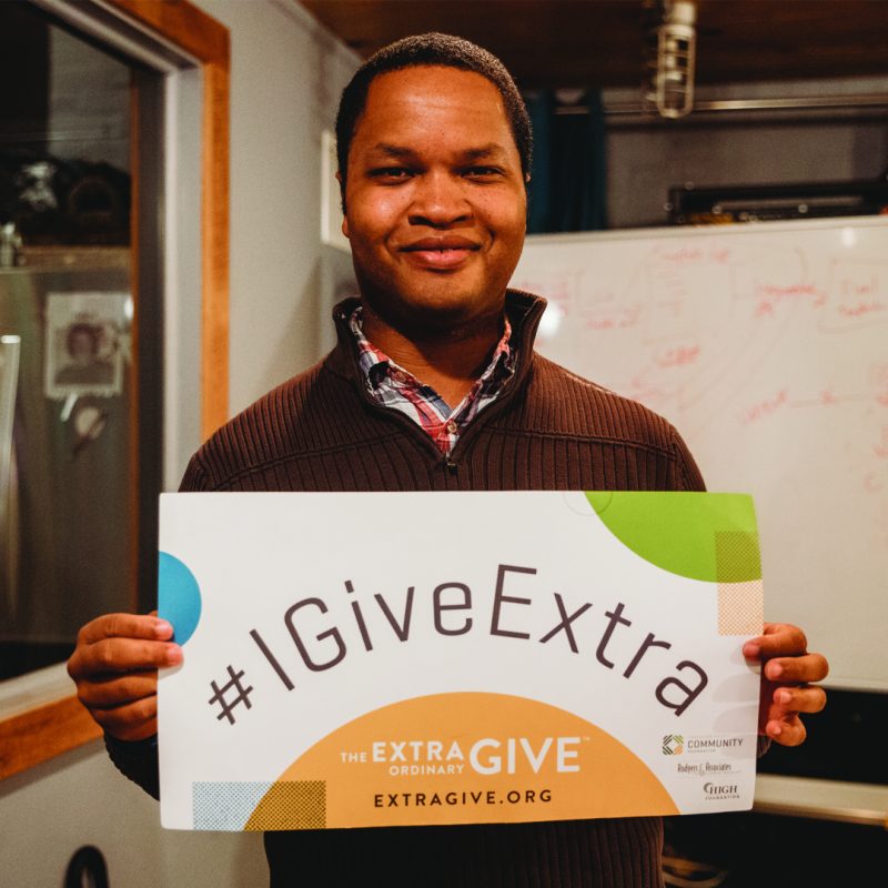 Photo of a man smiling while holding an extra give sign