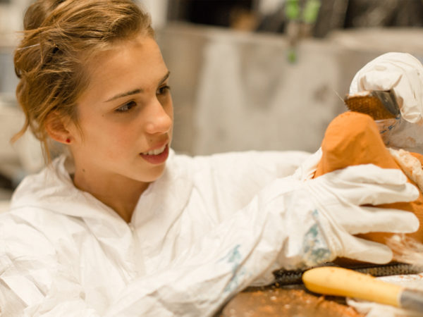 Young woman uses a tool to sculpt clay