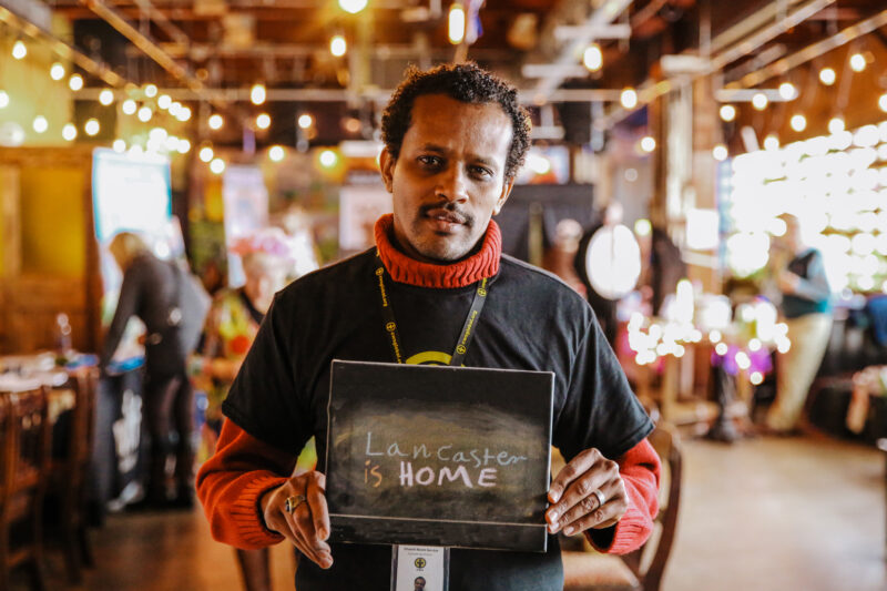 Lancaster resident and former refugee holding sign saying "lancaster is home"