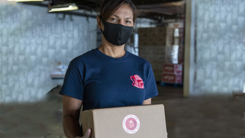 A masked woman poses for the camera while holding a box for Power Packs
